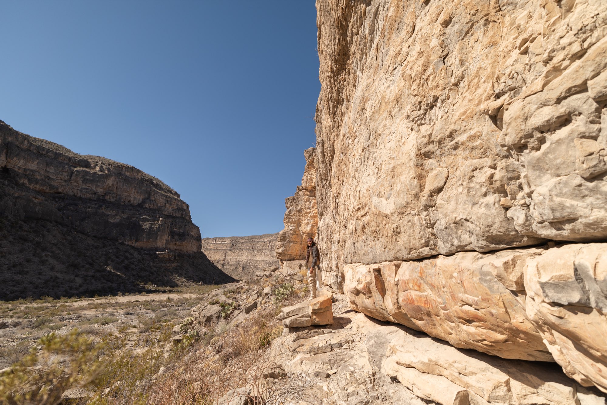 Persona diminuta bajo un enorme muro de roca en el cañón