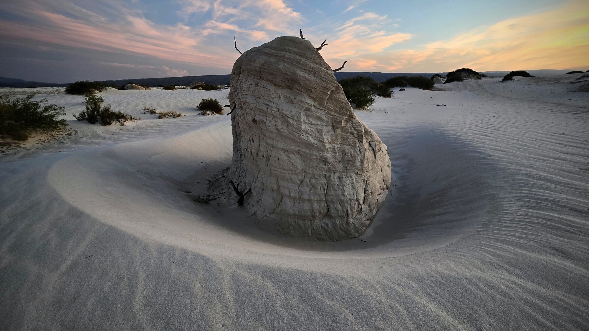 Roca erosionada sobre dunas de yeso blanco al atardecer