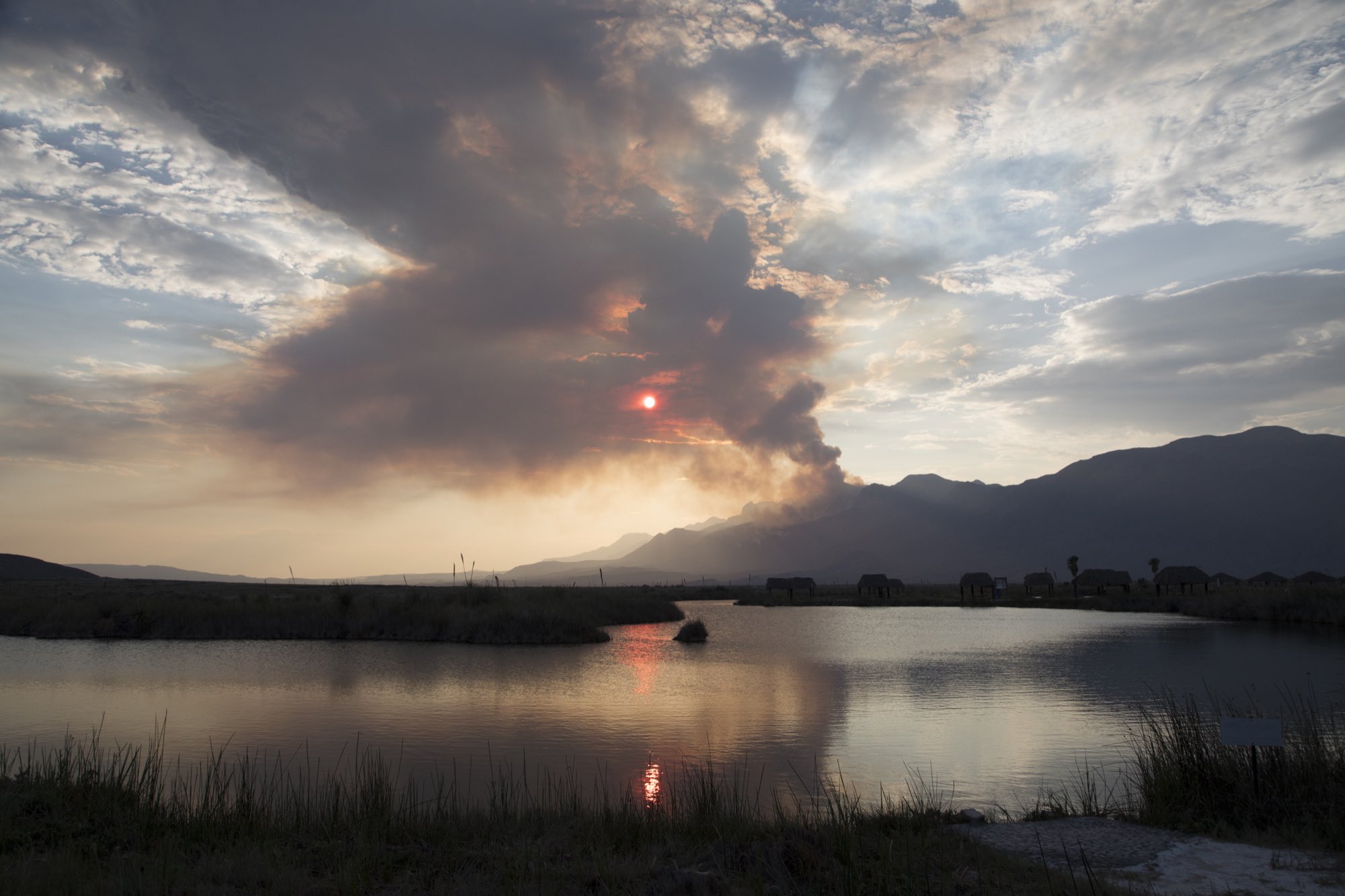 Atardecer nublado con sol rojo sobre la sierra reflejado en una poza