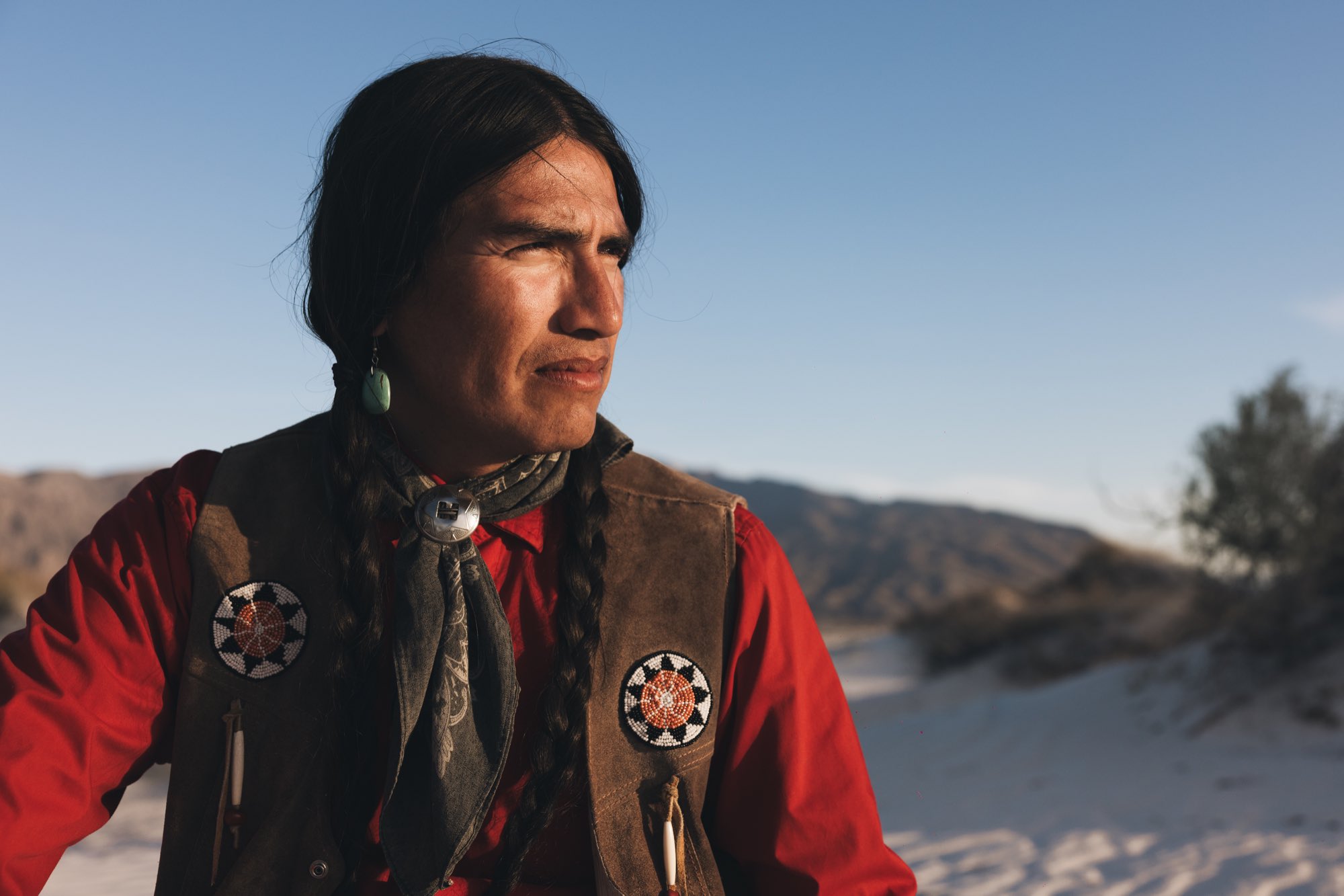 Retrato de hombre con trenzas y chaleco con abalorios frente al desierto