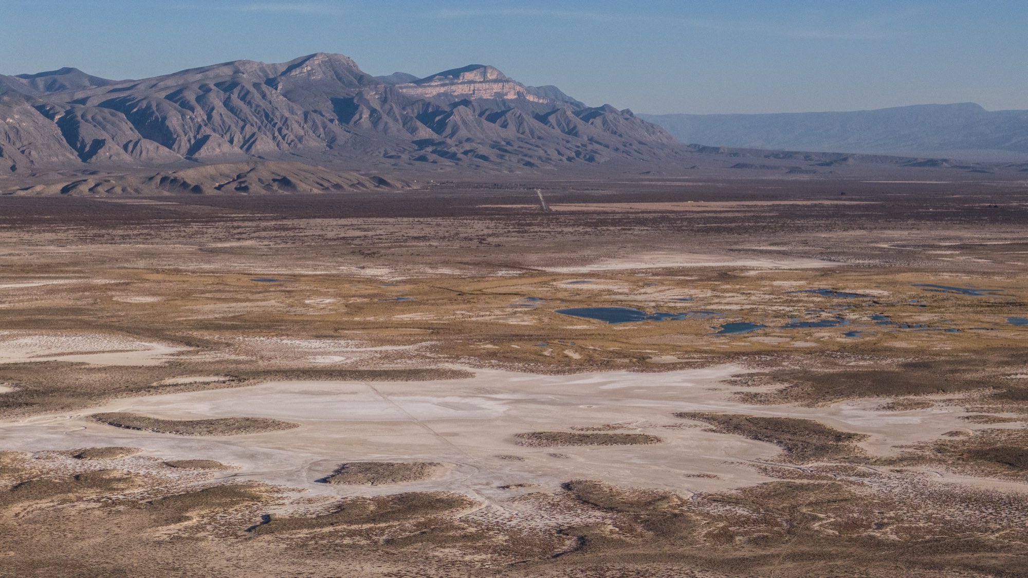 Vista aérea del valle desértico con pozas dispersas y sierra al fondo